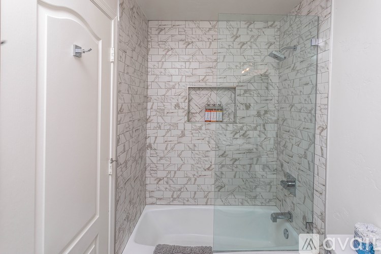 A white bathroom with a glass shower door and a marble tile wall.