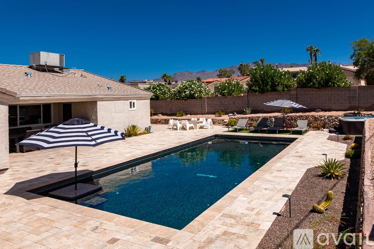 A pool with a striped umbrella and a house in the background.