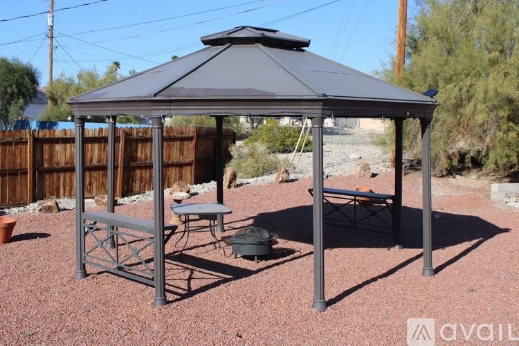 A gazebo with a table and chairs is set up in a backyard.