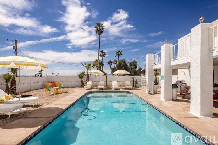 A pool with a white umbrella and chairs in front of a white building.