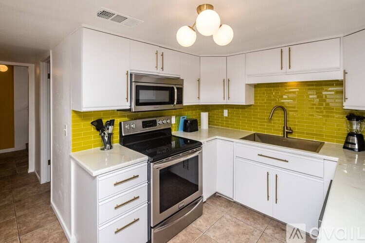 A kitchen with white cabinets and a green backsplash.