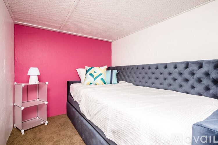 A bedroom with a bed, a pink wall, and a white lamp.