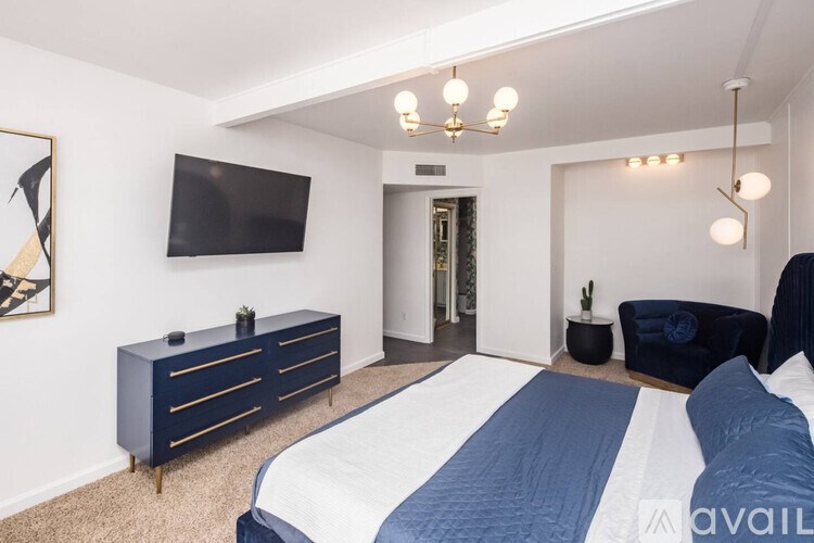 A bedroom with a bed, a blue sofa, and a TV mounted on the wall.
