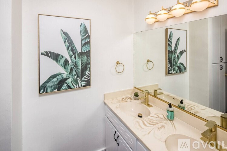 A bathroom with a white sink and a framed leafy picture on the wall.