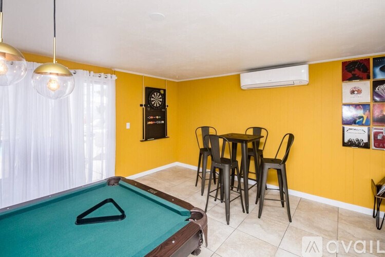 A pool table with a green felt cloth and a black triangle in the middle is in the foreground of a room with yellow walls.