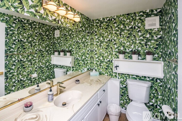 A bathroom with a green leafy wallpaper and a white toilet.