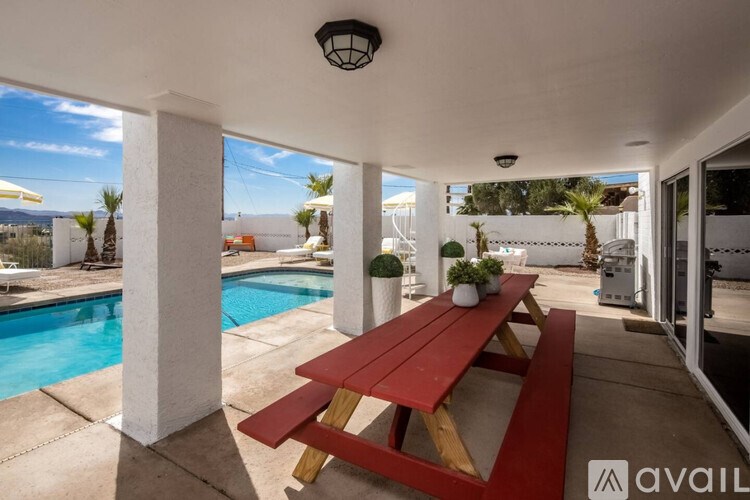 A red wooden table is in the middle of a patio with a pool.
