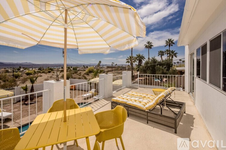A patio with a yellow table and chairs under a striped umbrella.