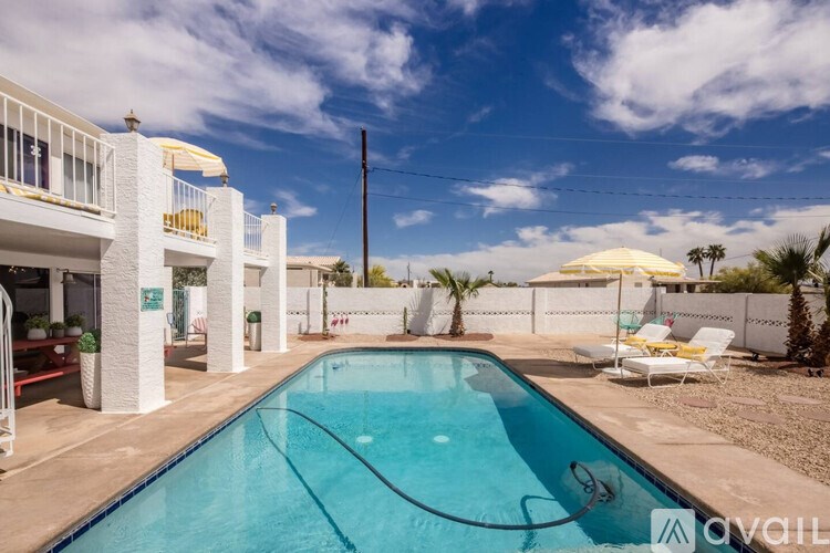 A pool in a sunny backyard with a white building and palm trees.