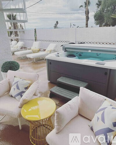 A poolside patio with a white couch, yellow table, and a hot tub.