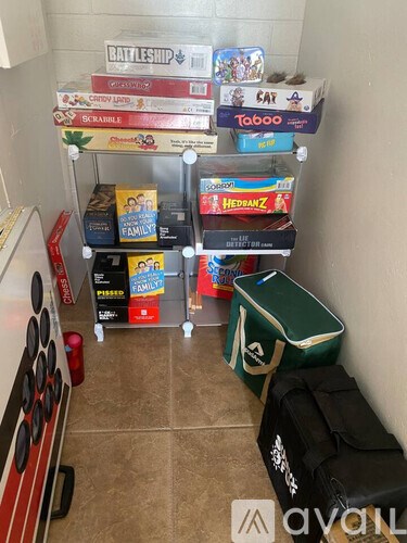 A room with a shelf full of board games and a green storage box on the floor.