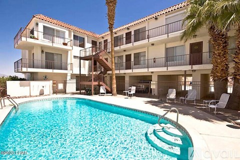 A large swimming pool is in front of a white building with a balcony.