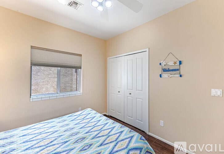 A bedroom with a bed, a window with blinds, a white door, and a wall hanging.
