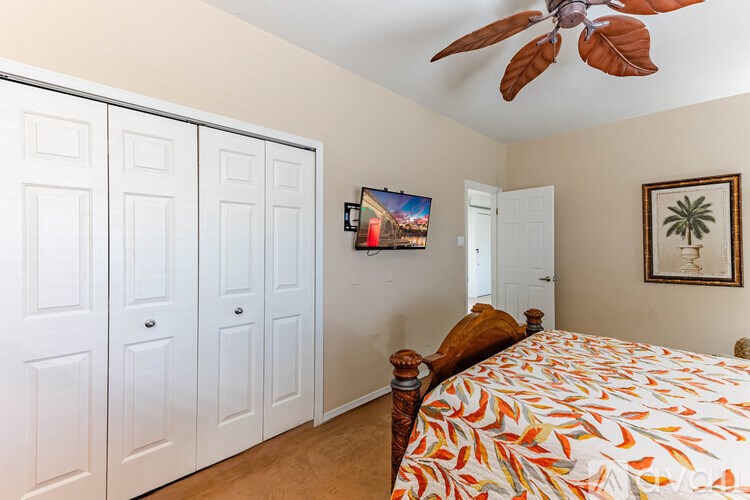 A bedroom with a bed, a ceiling fan, and a painting on the wall.