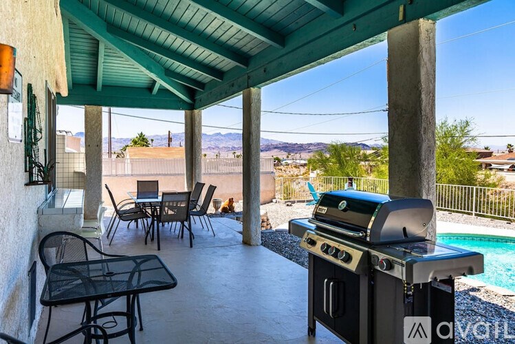 A patio with a grill and chairs overlooking a pool and mountains.