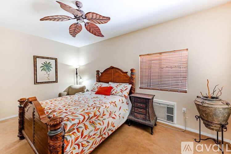 A bedroom with a bed, a ceiling fan, and a painting on the wall.
