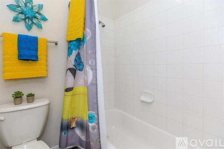 A bathroom with a white toilet, a yellow towel, a blue towel, a shower curtain with a flower design, and a starfish decoration on the wall.