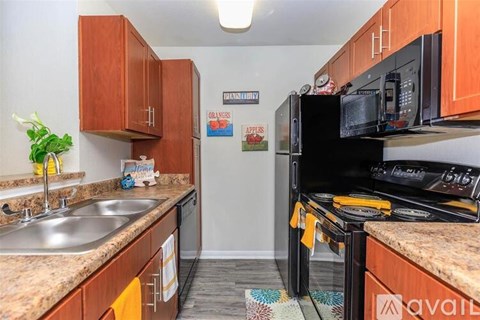 A kitchen with a black fridge and stove, wooden cabinets, and a granite countertop.