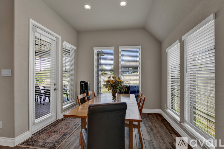 A dining room with a table and chairs and a vase of flowers on the table.