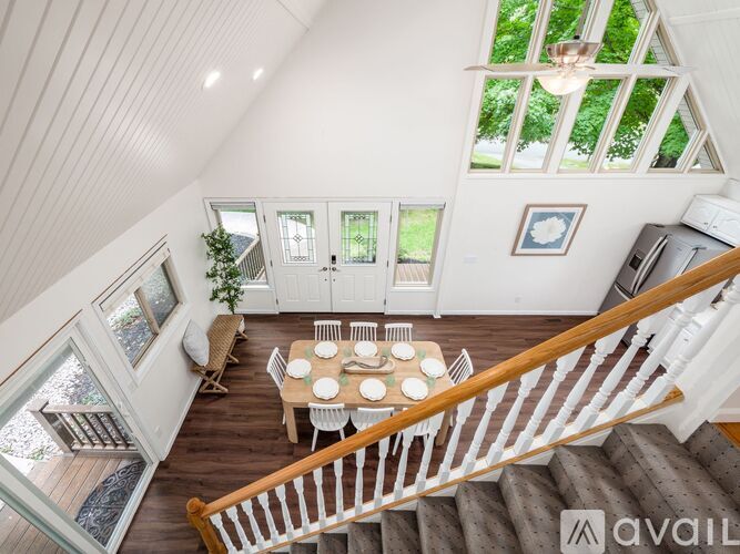 A white dining table with chairs is in the middle of a room with a staircase.