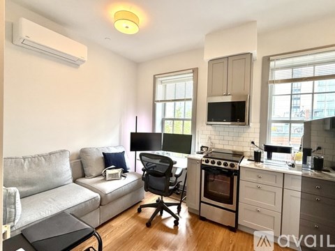 A well-lit kitchen and living room with a grey sofa and a black office chair.
