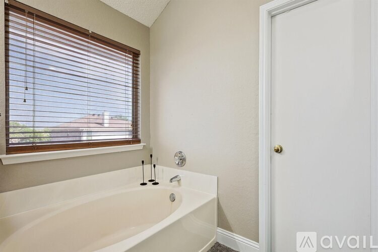 A bathroom with a white bathtub and a window with blinds.