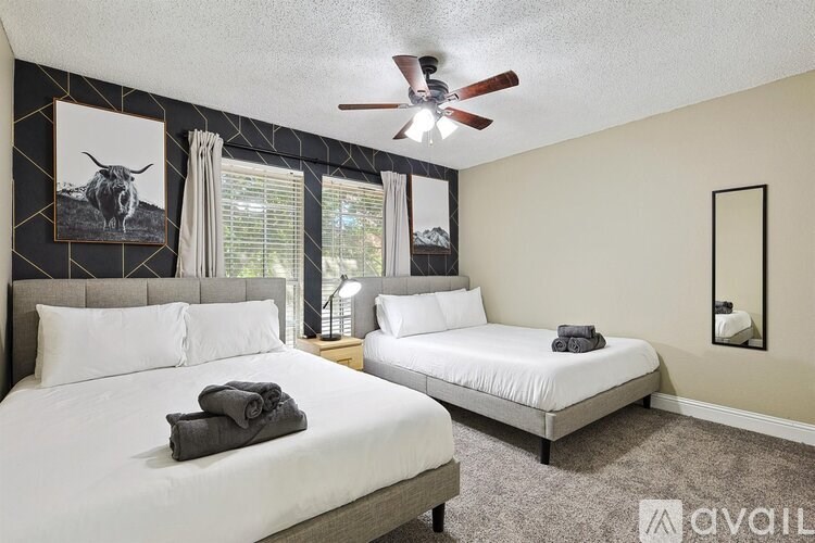 A bedroom with two beds, a ceiling fan, and a painting of a cow on the wall.