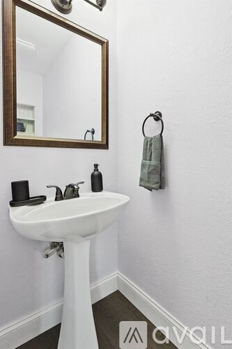 A white pedestal sink with a mirror above it and a towel hanging on the wall.