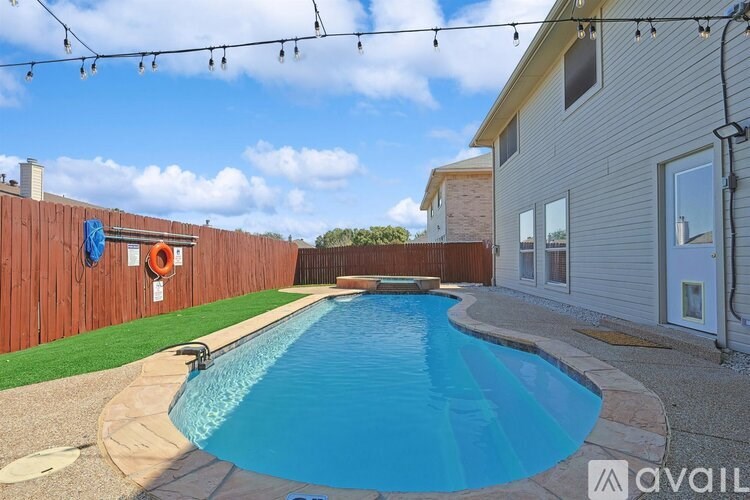A small residential pool surrounded by a wooden fence and a house.