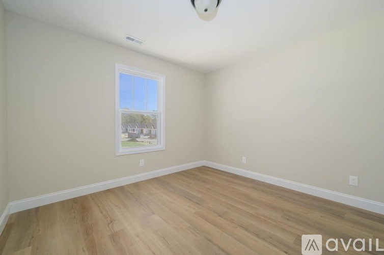 A room with wooden flooring and a window showing a view of trees.