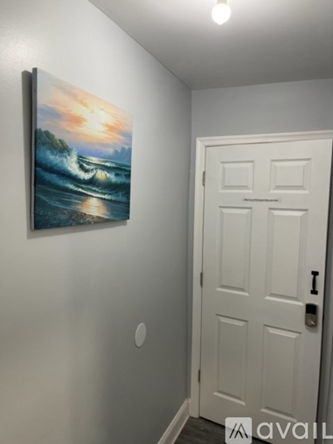 A painting of a sunset over the ocean is hanging on a white wall next to a white door.