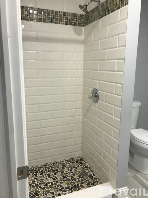 A white tiled shower with a silver shower head.