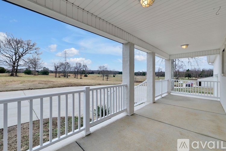 A porch with a white railing and a view of a field.
