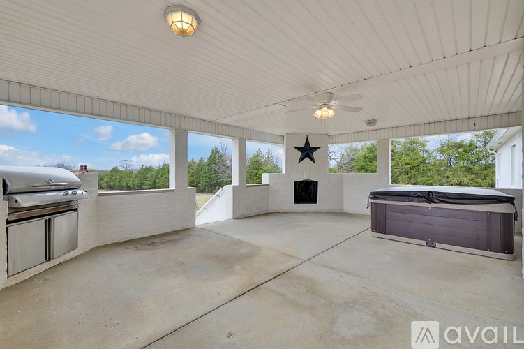 A spacious outdoor area with a grill, a hot tub, and a ceiling fan.