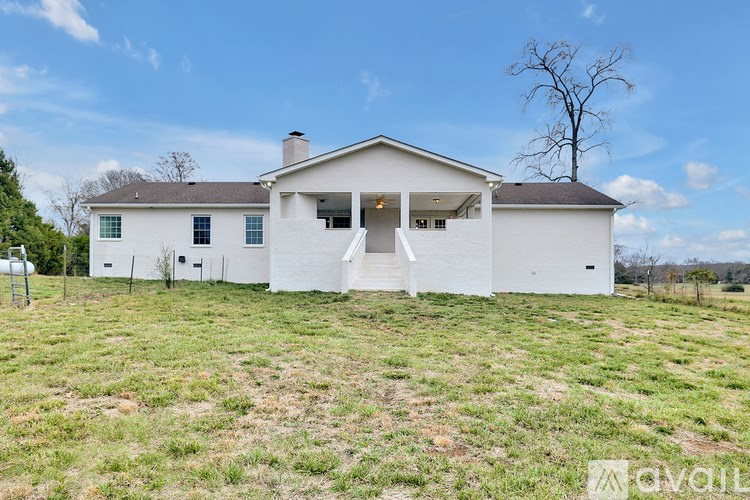 A white house with a black roof and a tree in front of it.