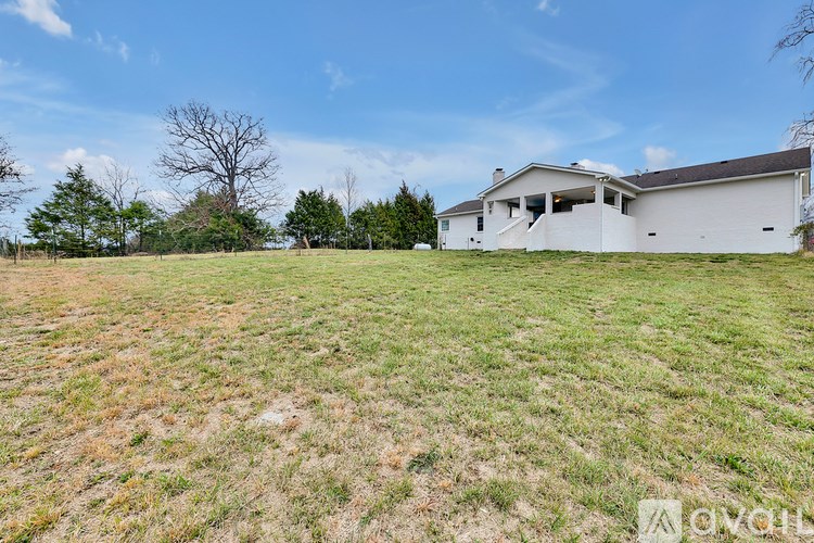 A large, open field with a house in the distance under a clear blue sky.