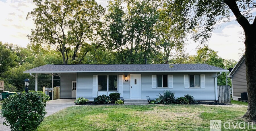 A house with a white door and windows is surrounded by greenery.