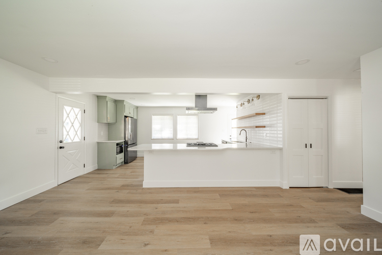 A spacious kitchen with wooden flooring and white walls.