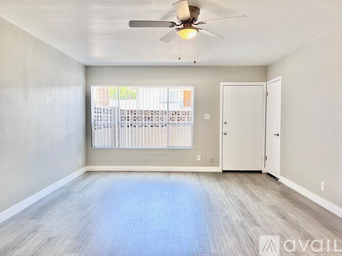 A spacious room with a ceiling fan and light, hardwood flooring, and a sliding glass door leading to a balcony.