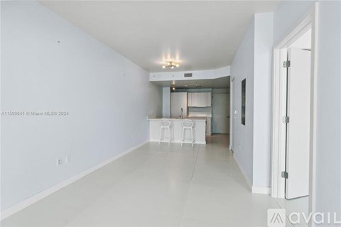 A spacious room with white walls and flooring, featuring a kitchen area with white cabinets and appliances.
