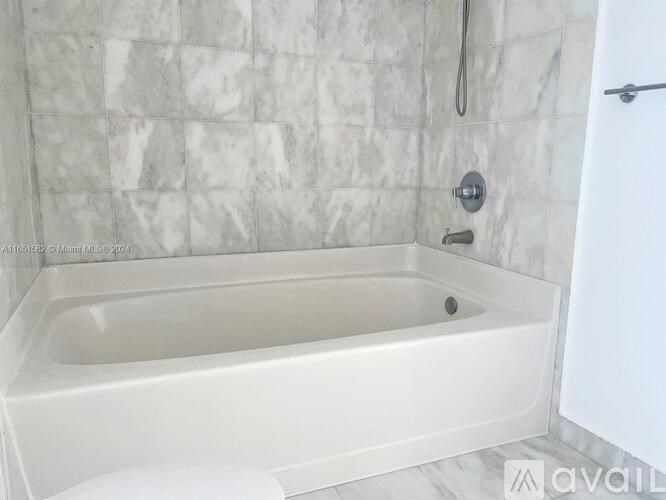 A white bathtub is in a bathroom with a marble tile wall.