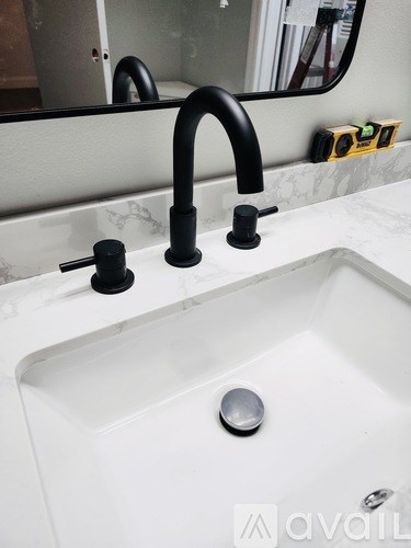 A white sink with a black faucet and a silver drain cover.