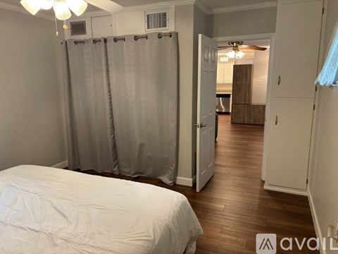 A bedroom with a bed, a shower curtain, and a wooden floor.