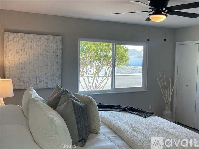 A bedroom with a bed, pillows, a ceiling fan, and a window with a view of trees.