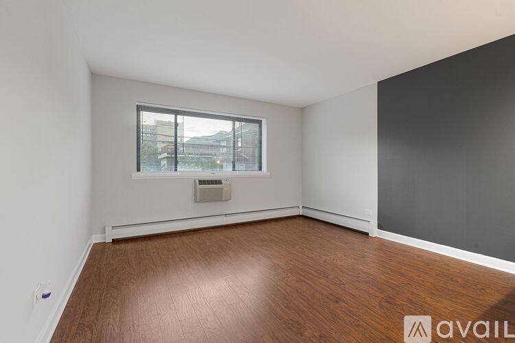 A room with wooden flooring and a window with a view of buildings outside.