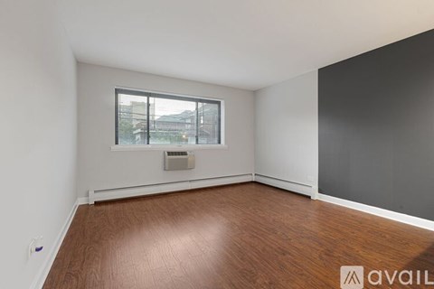 A room with wooden flooring and a window with a view of buildings outside.