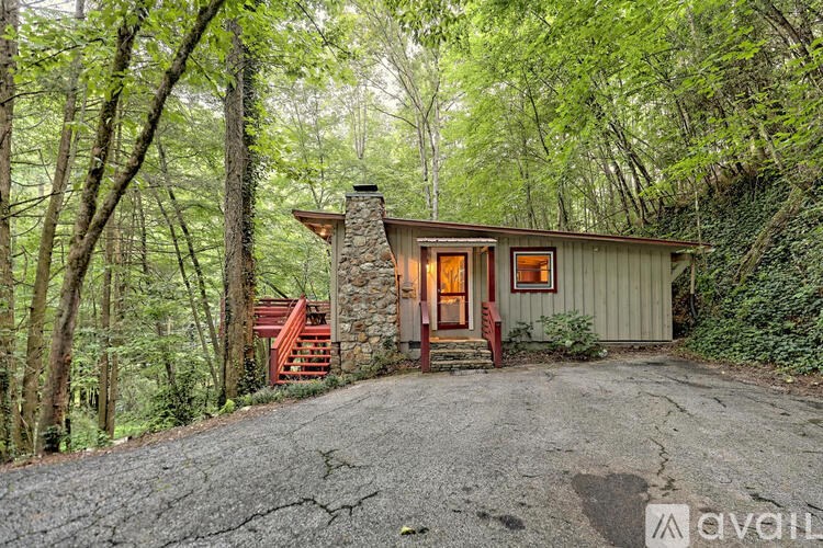A small house with a stone chimney is surrounded by trees.