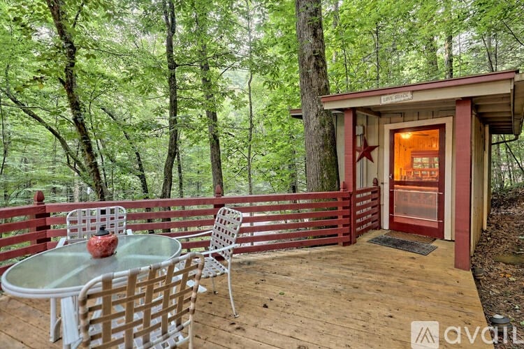 A small table and chairs are set up on a deck in front of a treehouse.