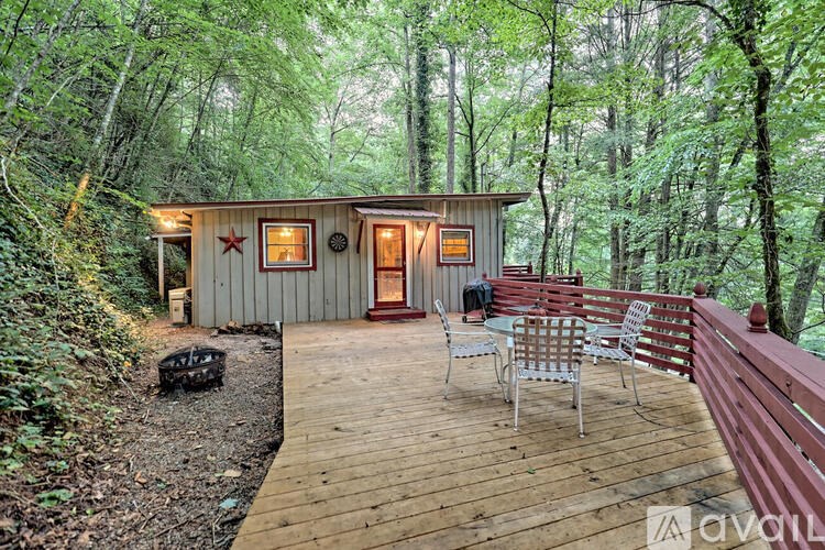 A wooden cabin with a deck and a red bench is surrounded by trees.