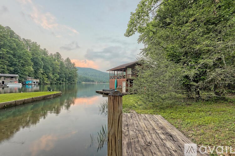 A wooden dock extends into a calm body of water with a house on the opposite shore.